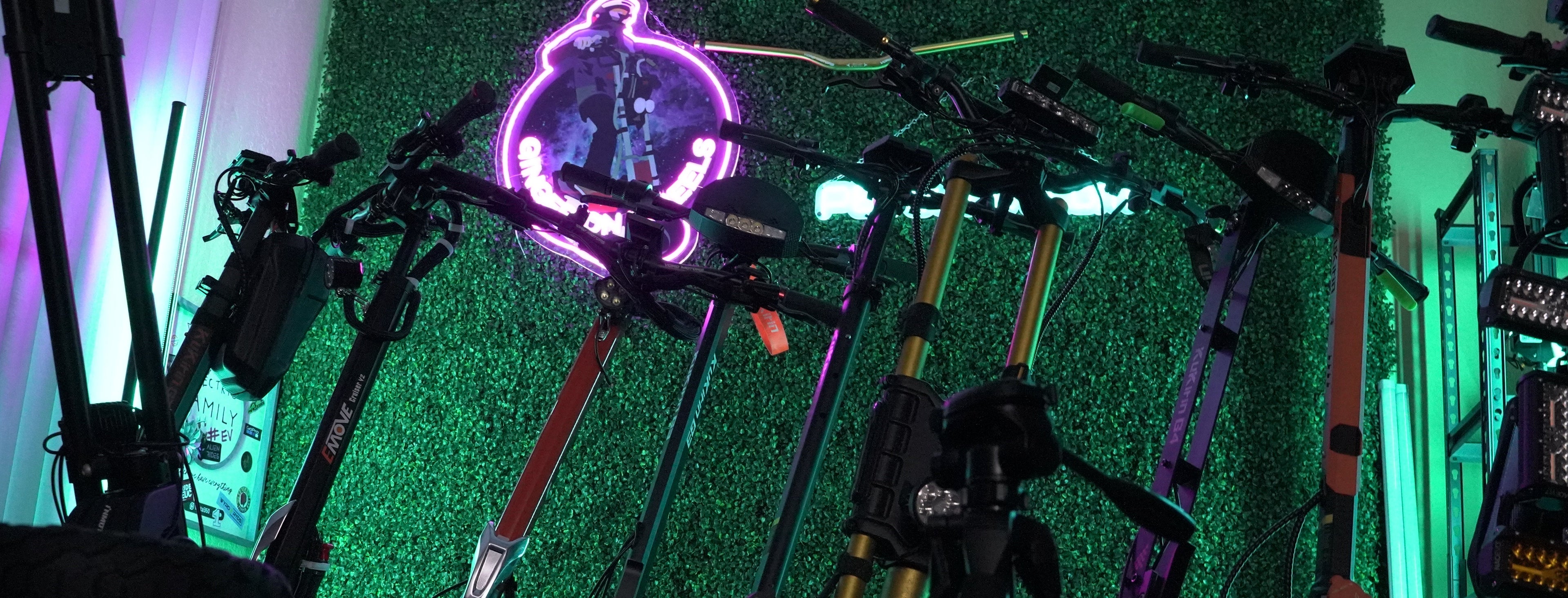 Multiple electric scooters with a LED sign lighting them from behind